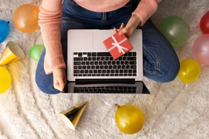 Pessoa sentada no chão com notebook e presente nas mãos, cercada por balões coloridos, simbolizando o benefício do saque-aniversário do FGTS como forma de celebração e alívio financeiro.